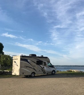 Small tan and white class B RV parked in front of the ocean