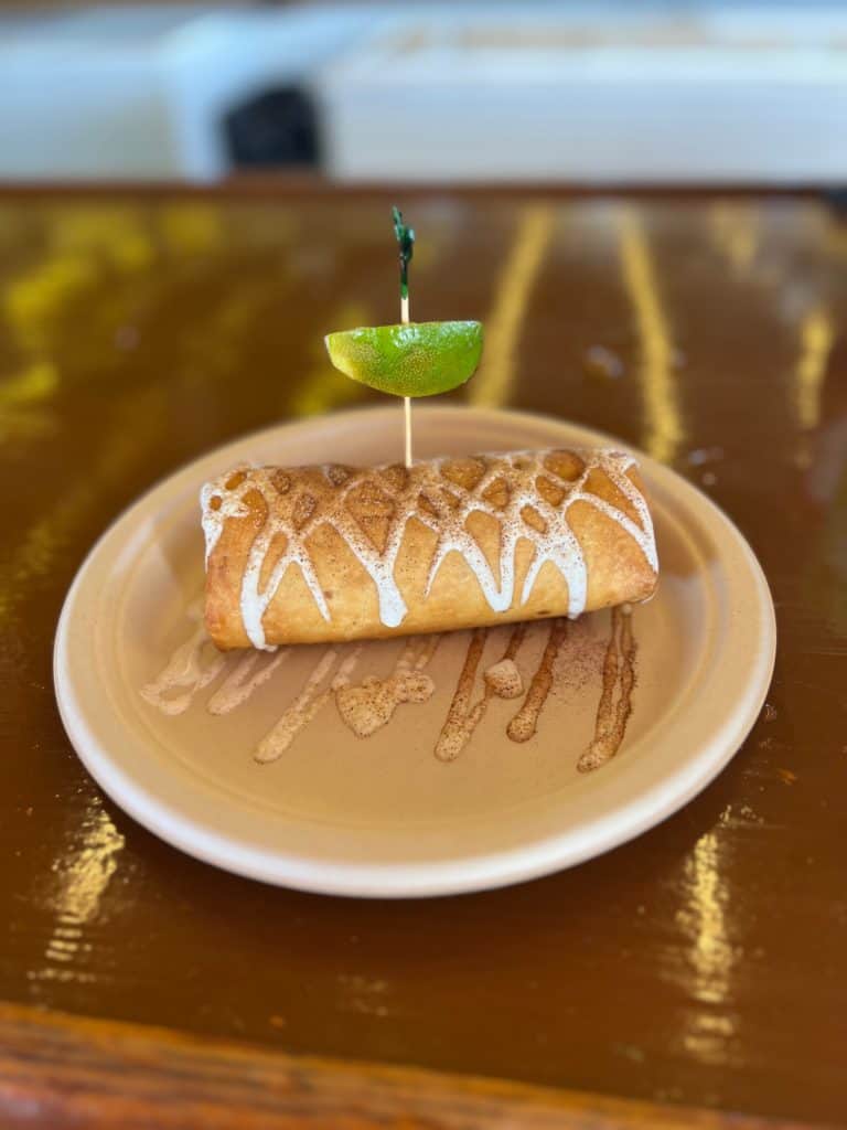 image of a golden burrito-like fried key lime pie on a plate with a lime on a toothpick on top