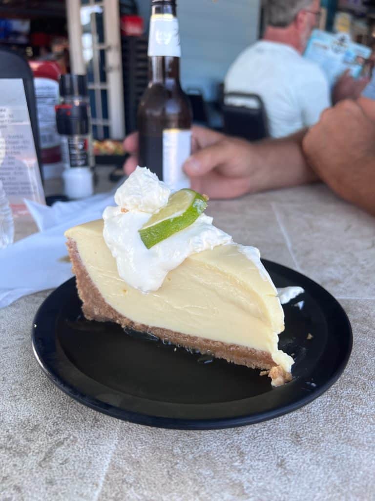Picture of a large piece of key lime pie with graham cracker crust on a plate at a restaurant table