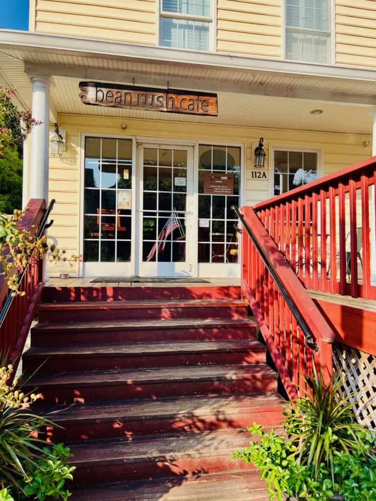 Yellow building with reddish deck and stairs. Outside deck and entrance to Bean Rush Cafe coffeeshop in West Annapolis, MD.
