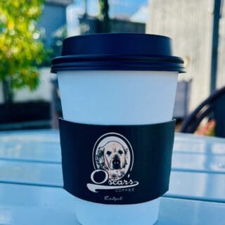 A to go cup of coffee in a black and white cup with the Oscar's logo on it.