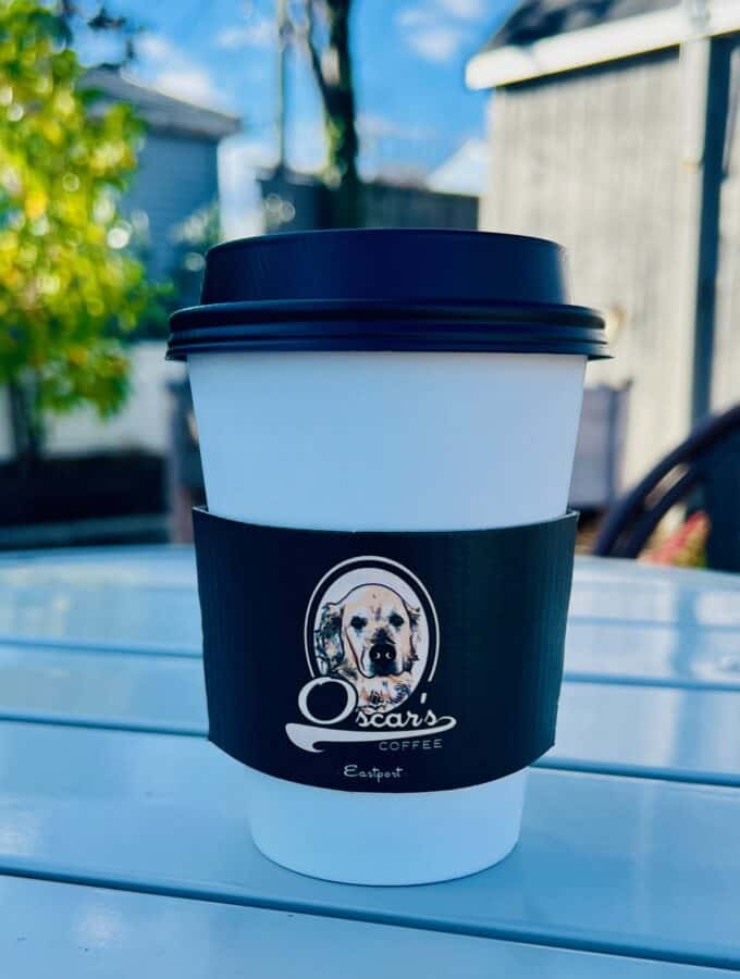 A to go cup of coffee in a black and white cup with the Oscar's logo on it.