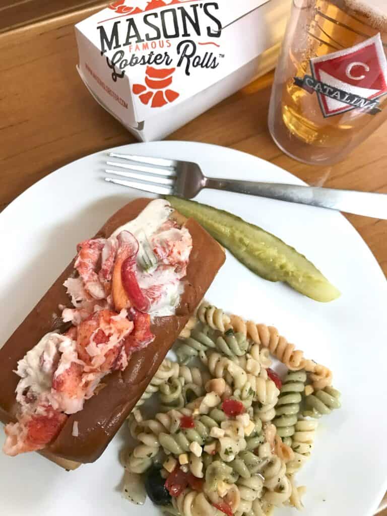 Lobster Roll on a plate with a pickle and a side of pasta salad