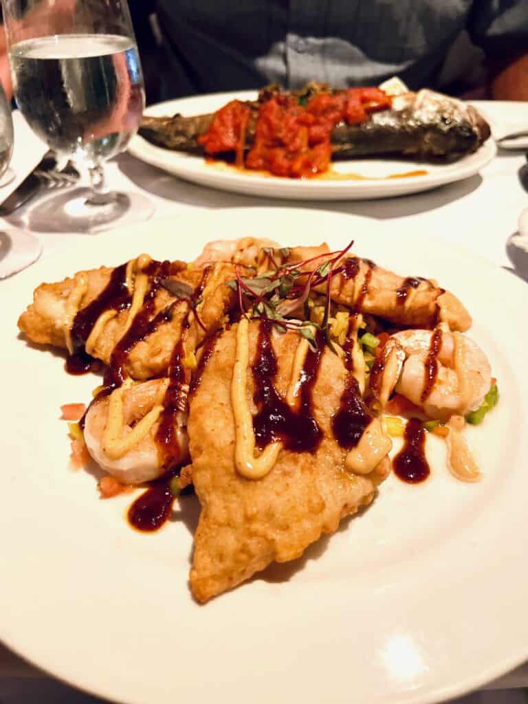 Fried fish on a white plate with a sauce drizzled over it
